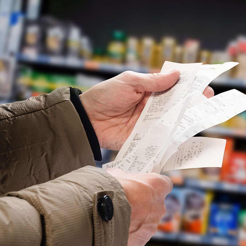 Man in supermarket holding sheaf of receipts